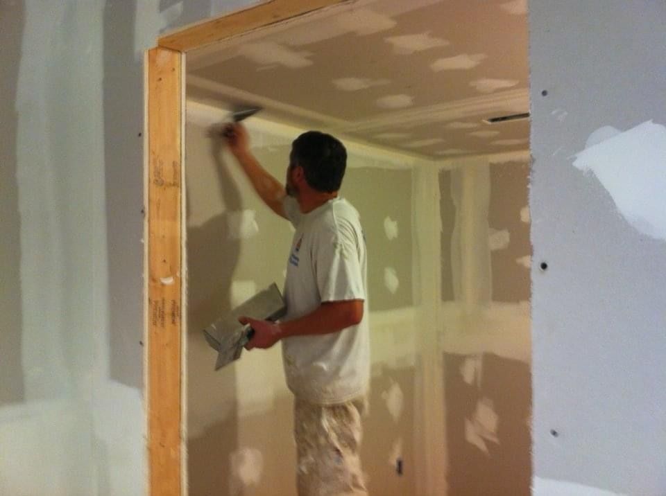 Crew member finishing drywall seams on a new wall