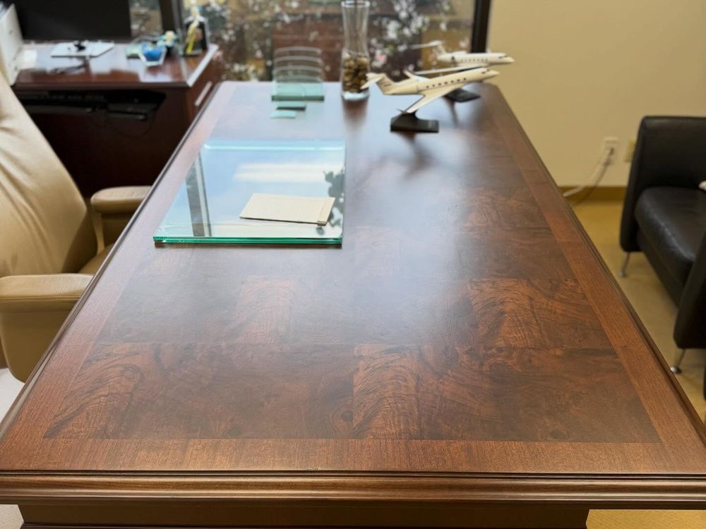 Large wood desk with a burl-veneer top in a banded border pattern, a glass desk pad and a model jet on it, in an office