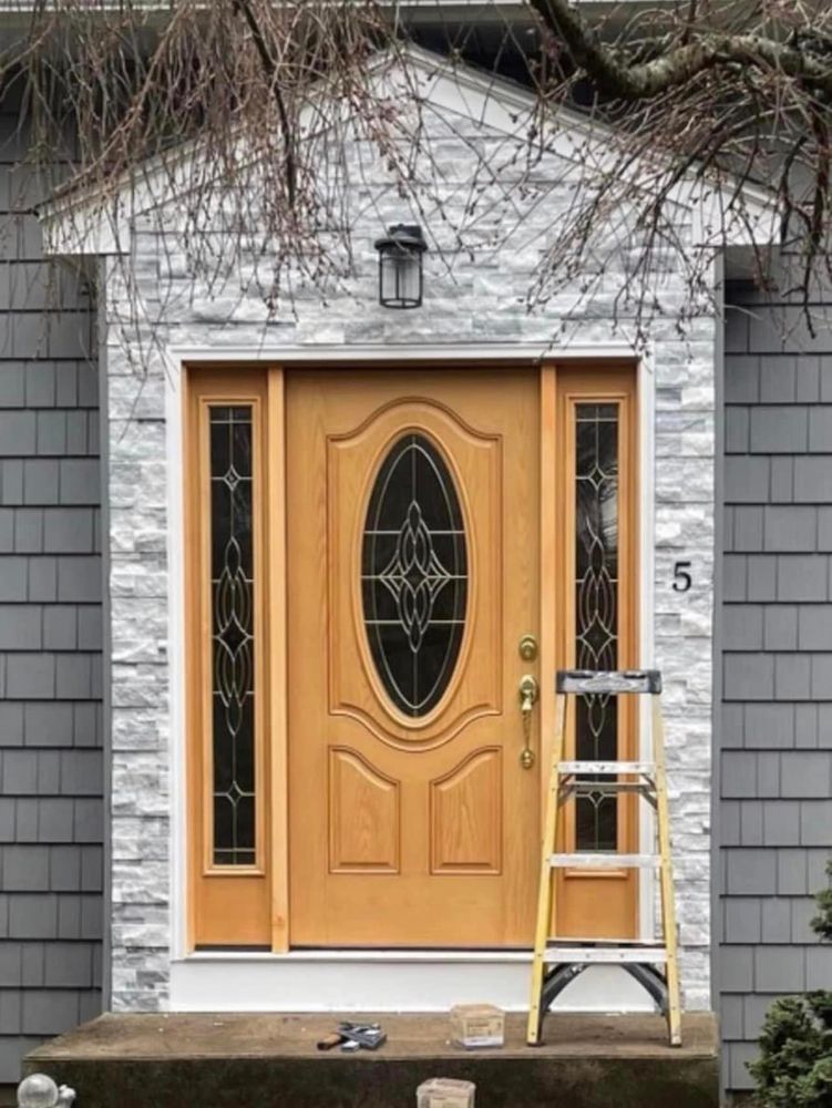 New wood entry door set into a stone veneer surround with shingle siding