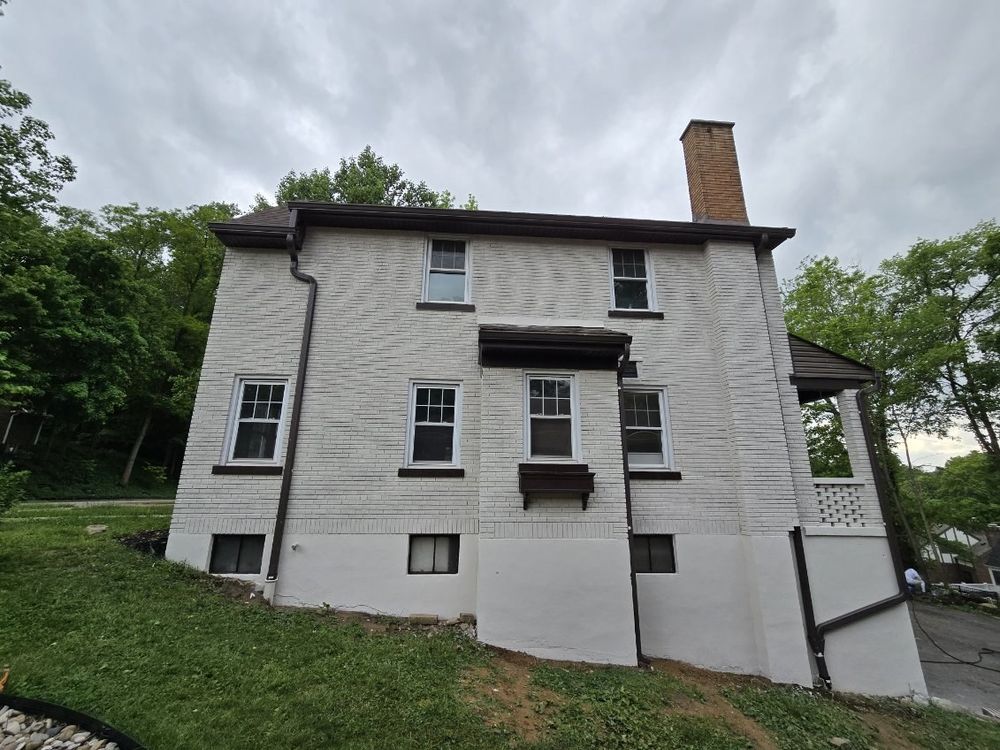 Light gray hillside home with dark trim and gutters, repainted by Slye's Painting