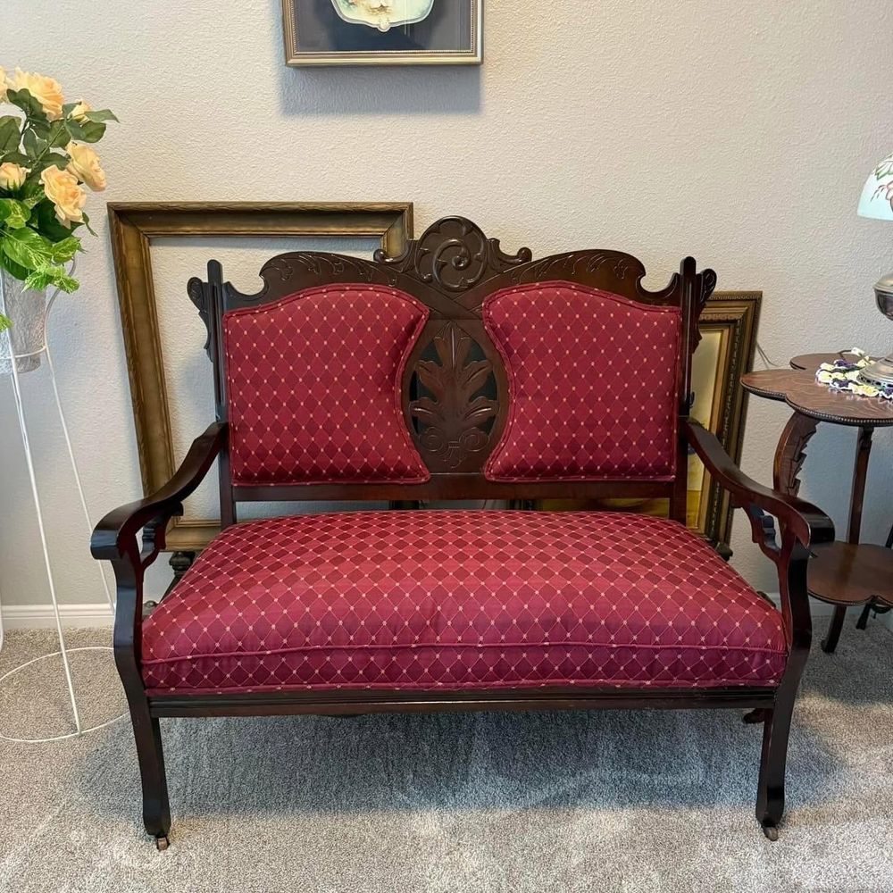 Carved dark-wood loveseat with red diamond-pattern upholstery in front of antique picture frames