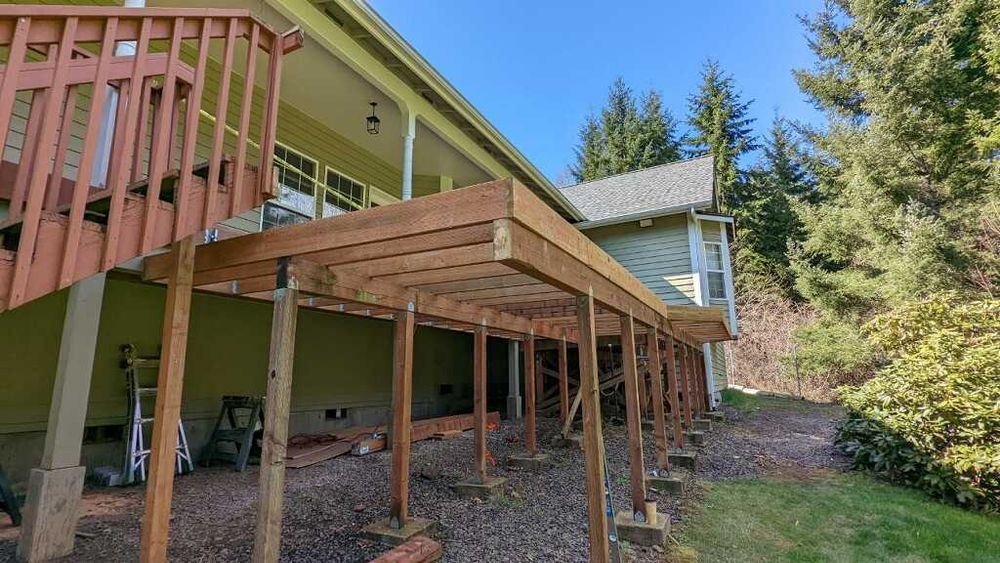 EVERGREEN...

Ben and Cynthia's country home sparkled in the sunlight that is until you took a look at their weathered and rotting back deck. As a couple they enjoyed the peace of the outdoors but the deck was sorrowful. A call to Racketty Boom would solve the problem.

The old wooden deck was stripped away. Rotted posts and beams were replaced to support a new composite decking and railing system. Keeping with the theme of evergreens surrounding their home, the couple chose green with white trim. Now when the couple sit outside they feel only tranquility that nature provides and peace of mind in the beauty of their new deck. for Racketty Boom Construction  in Centralia, WA