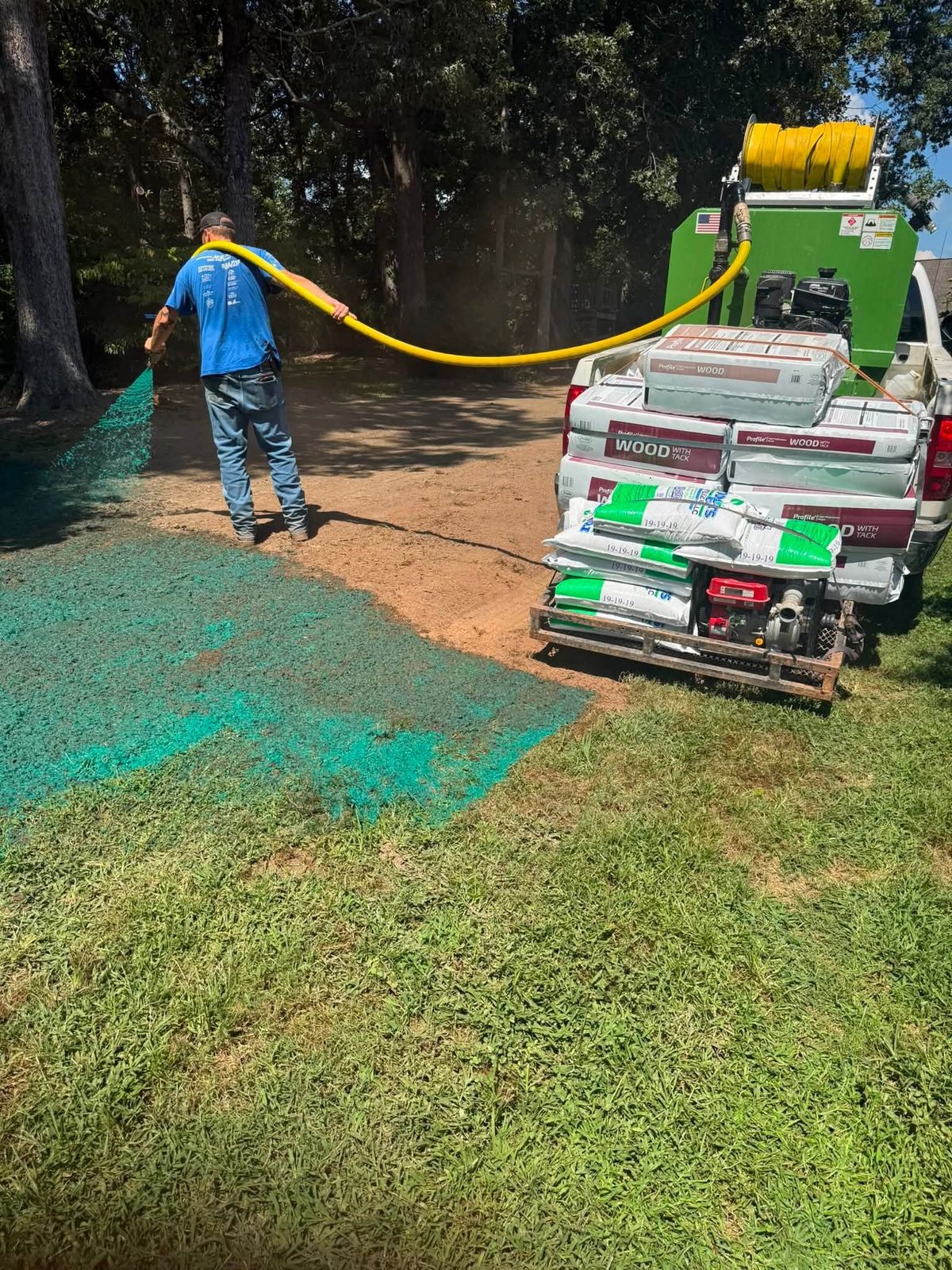 Crew member spraying green hydroseed mulch from a truck-mounted hydro mulcher onto a yard