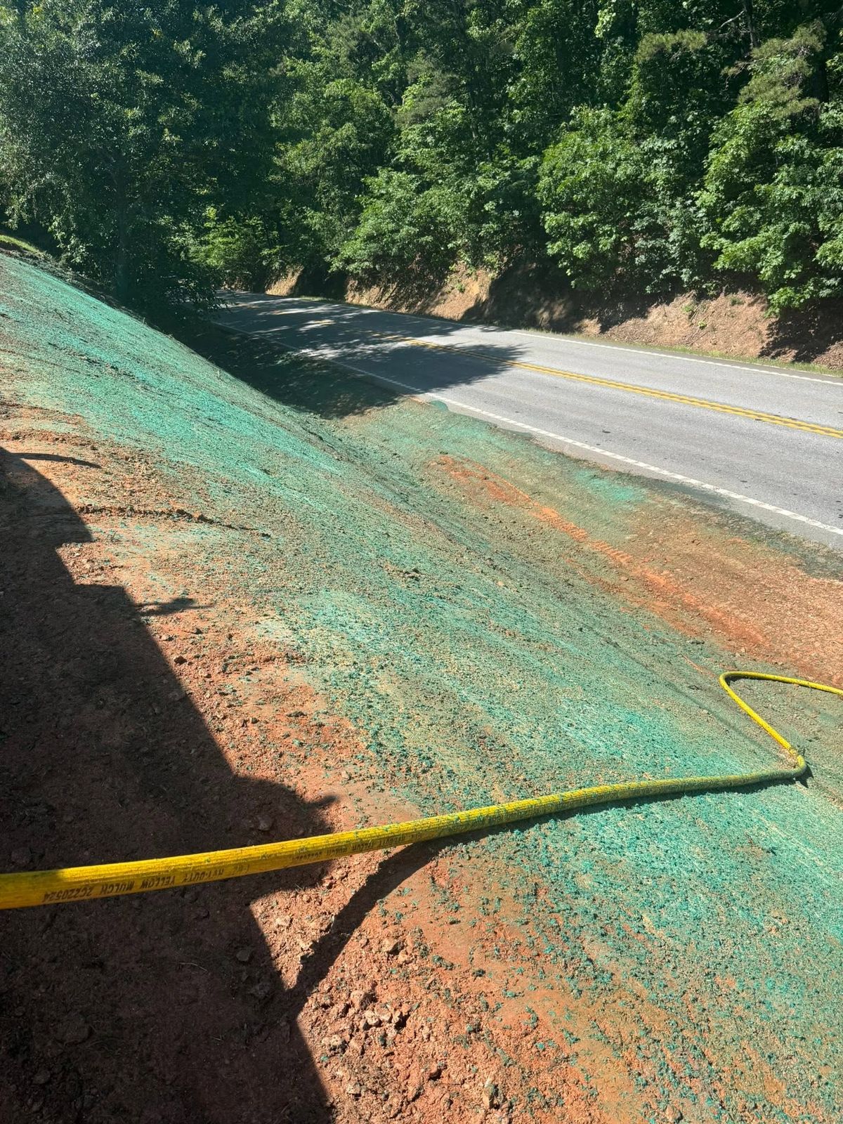 Hose laid across a freshly sprayed roadside slope beside a two-lane road