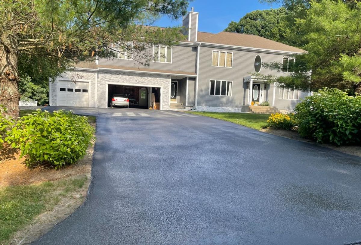 New asphalt driveway curving up to a large home with an open two car garage