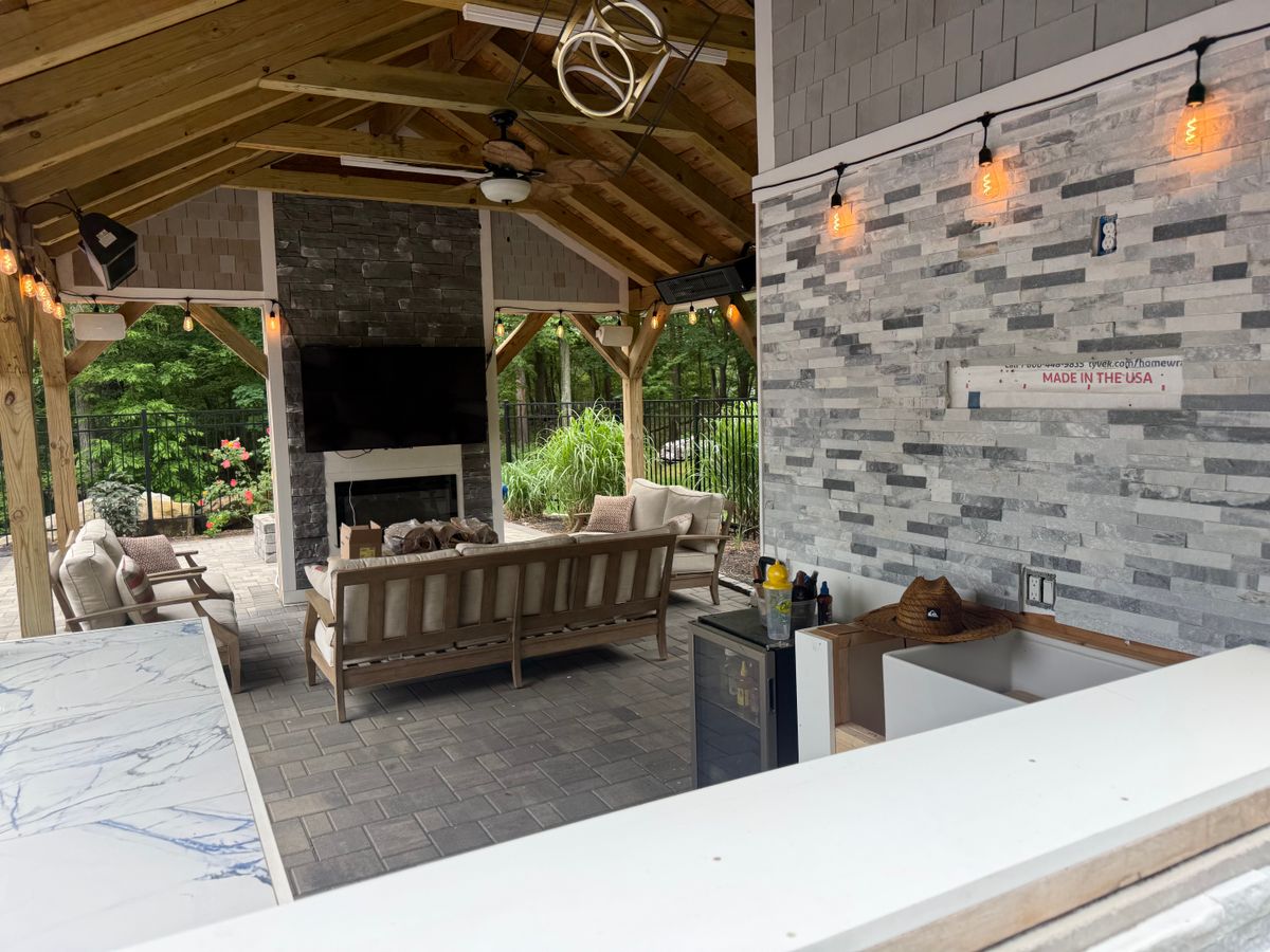Covered outdoor pavilion with a stone fireplace, stacked stone bar and string lighting