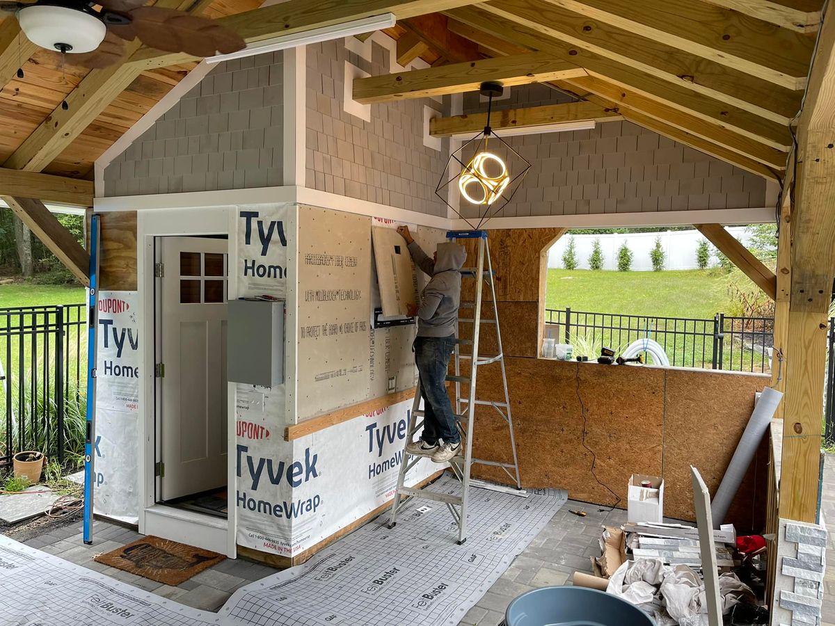Carpenter installing house wrap over new framing on a timber framed covered structure