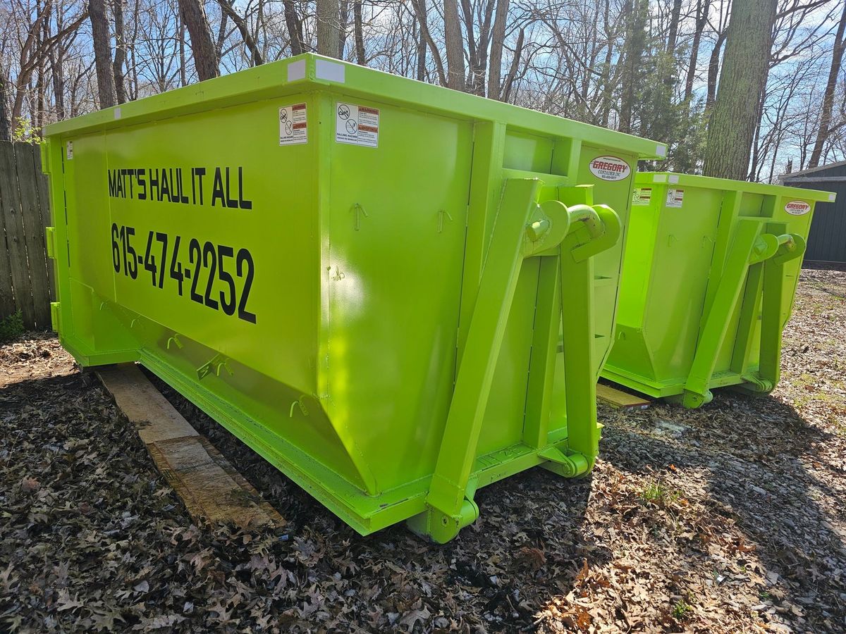Two bright green Matt's Haul it All roll-off dumpsters on a wooded lot
