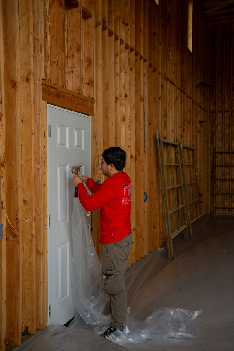 Foam Pro Insulation technician in a red shirt masking a door with plastic sheeting inside a wood-framed building before insulation work