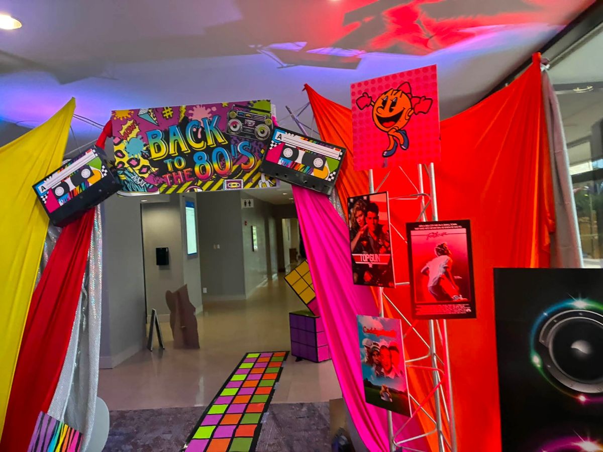 Back to the 80s themed entrance with bright draped fabric, cassette signs, and a light-up dance floor path