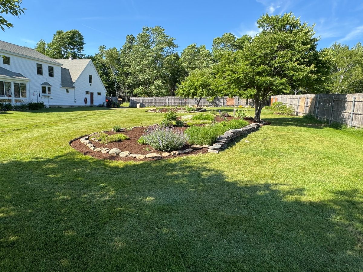 Curved stone edged planting bed running along the edge of a lawn
