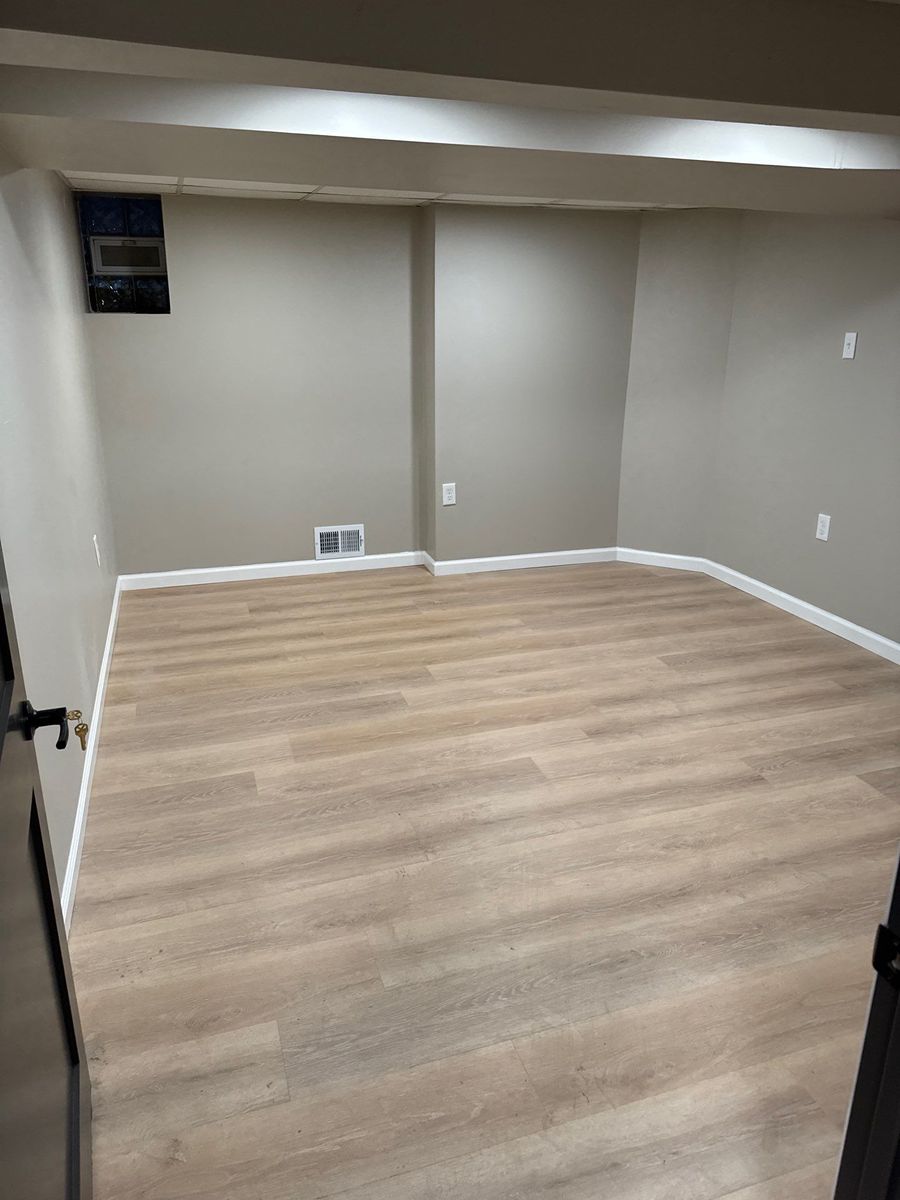 Finished basement room with wood-look flooring, gray walls and white baseboards