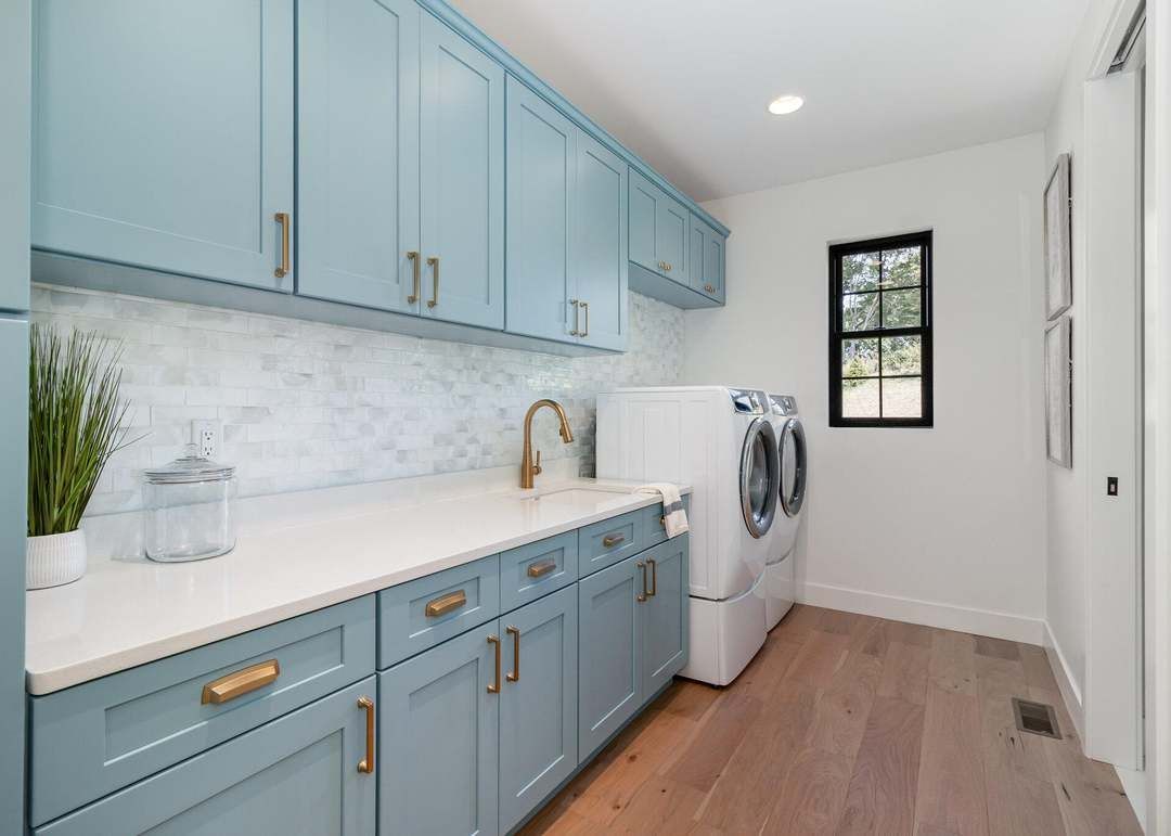 Finished blue painted cabinets with brass pulls in a bright laundry room