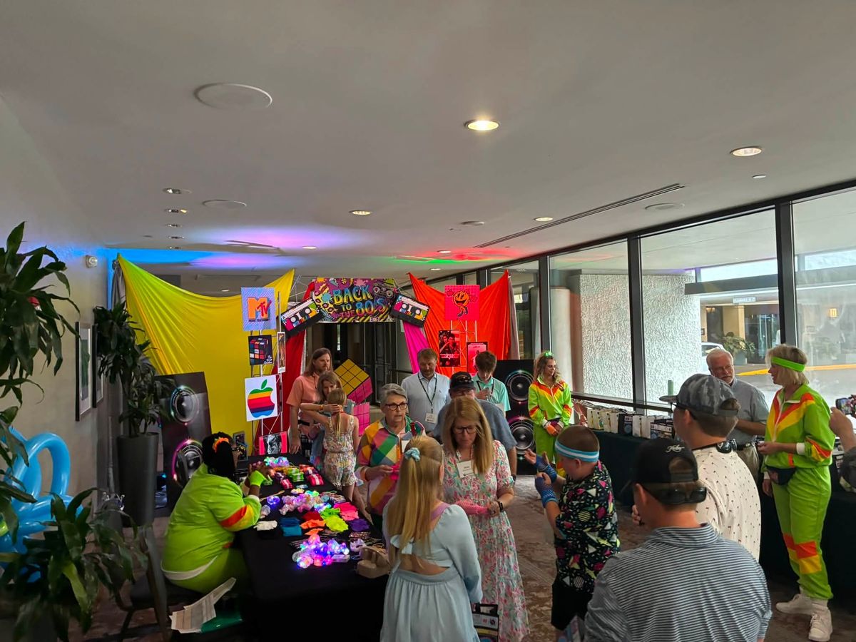 Guests in 80s costumes gathered around a themed photo booth and props table