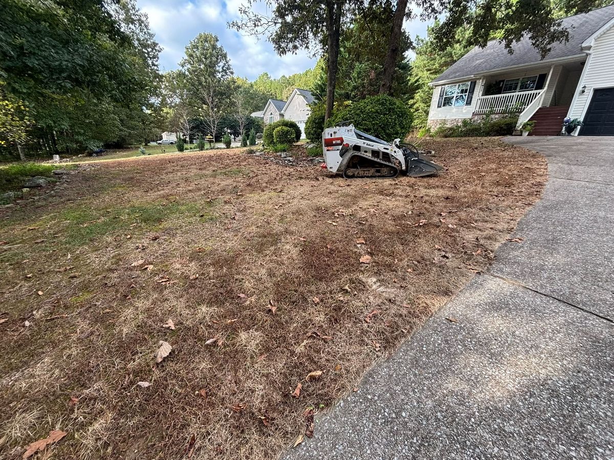 Front yard with dead grass and pine needles before sod, with a skid steer on site