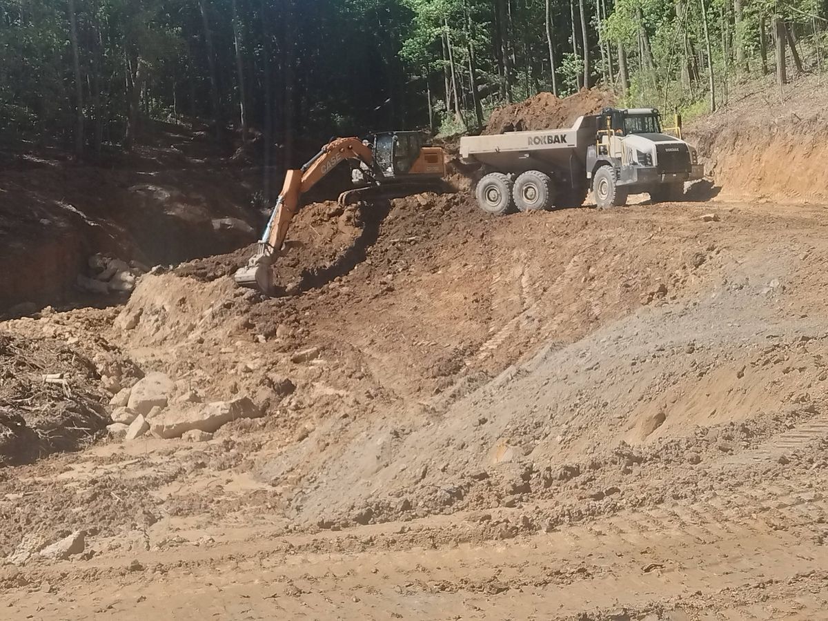 Excavator loading an articulated dump truck on a dirt job site in the woods