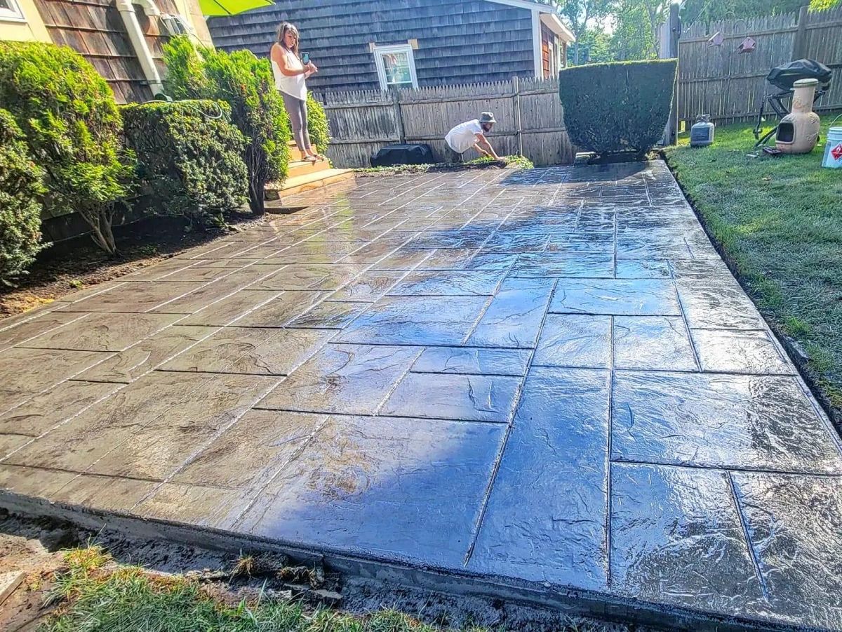 Freshly sealed ashlar pattern stamped concrete patio in a fenced back yard