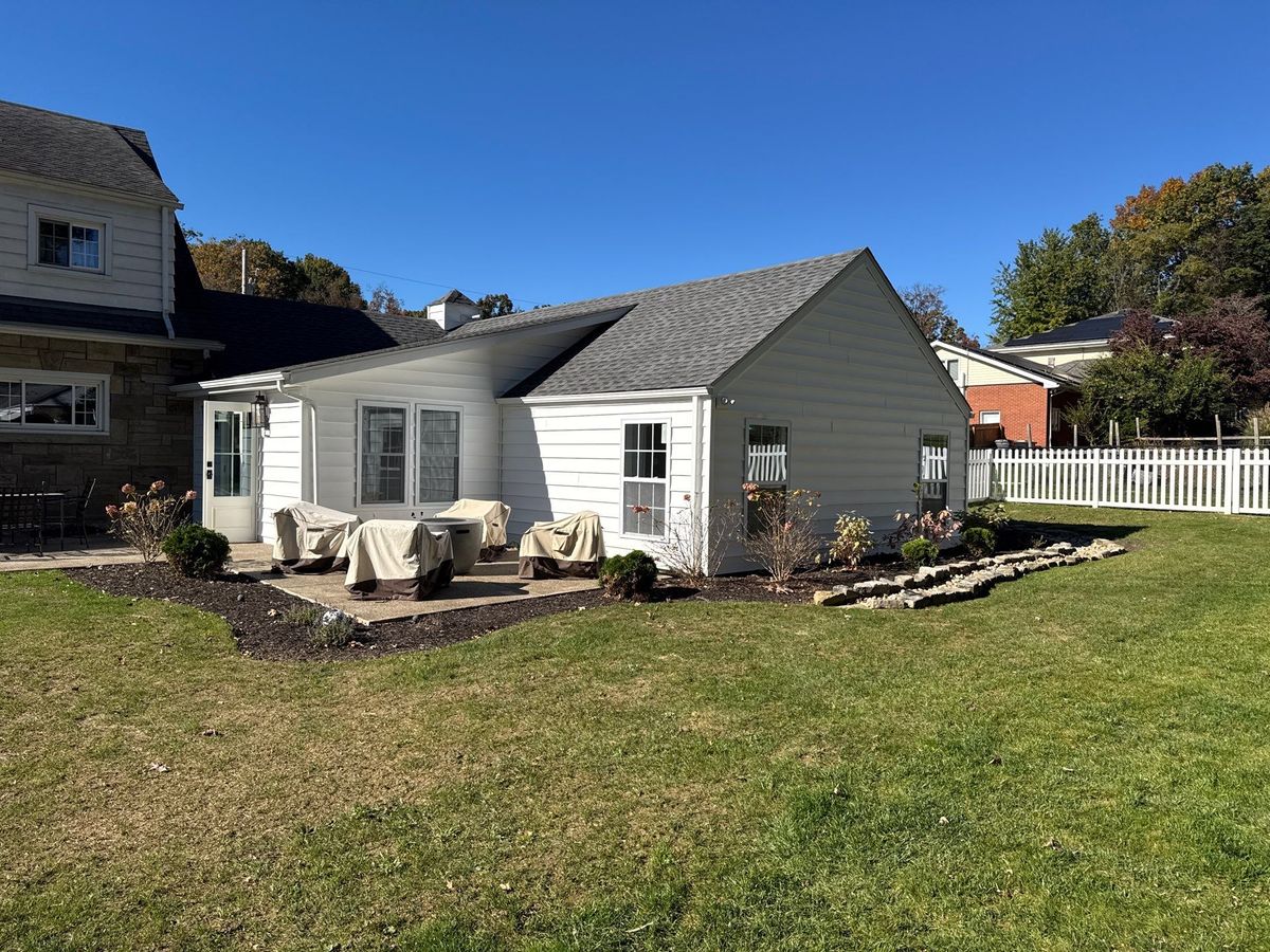 Finished home addition seen from the backyard, with a gray shingle roof and a patio