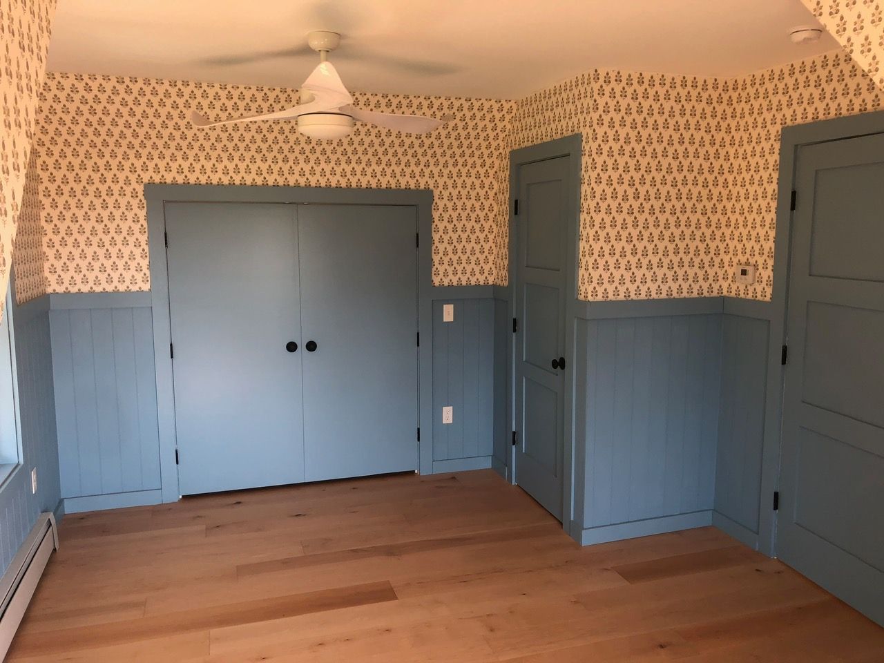 Bedroom with blue double closet doors, wallpaper and beadboard wainscot