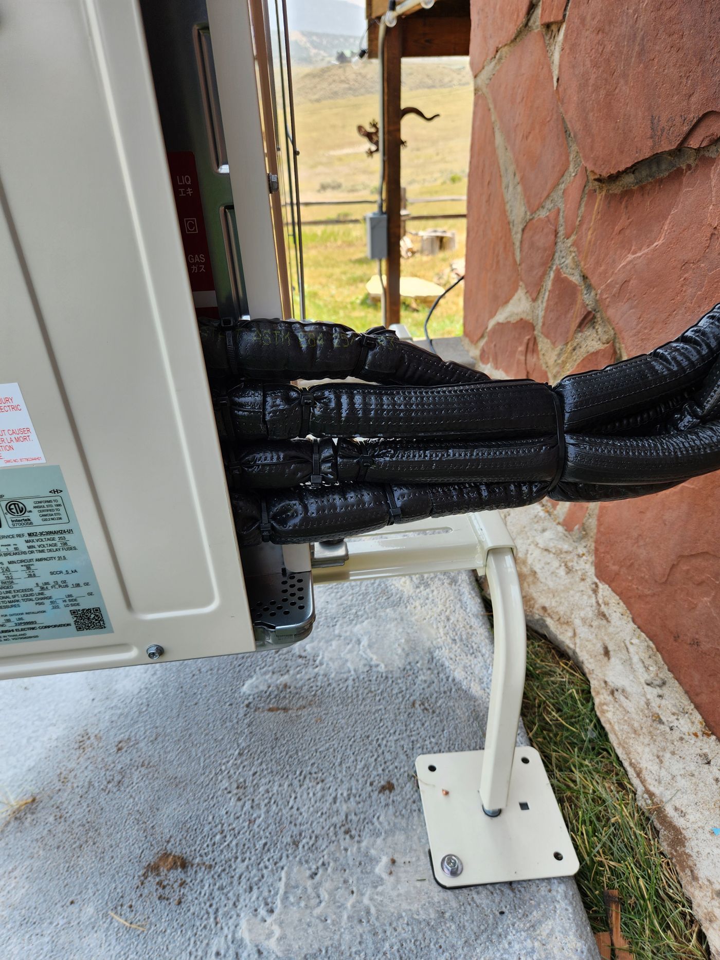 Insulated line set entering a condenser on a wall stand against a stone wall