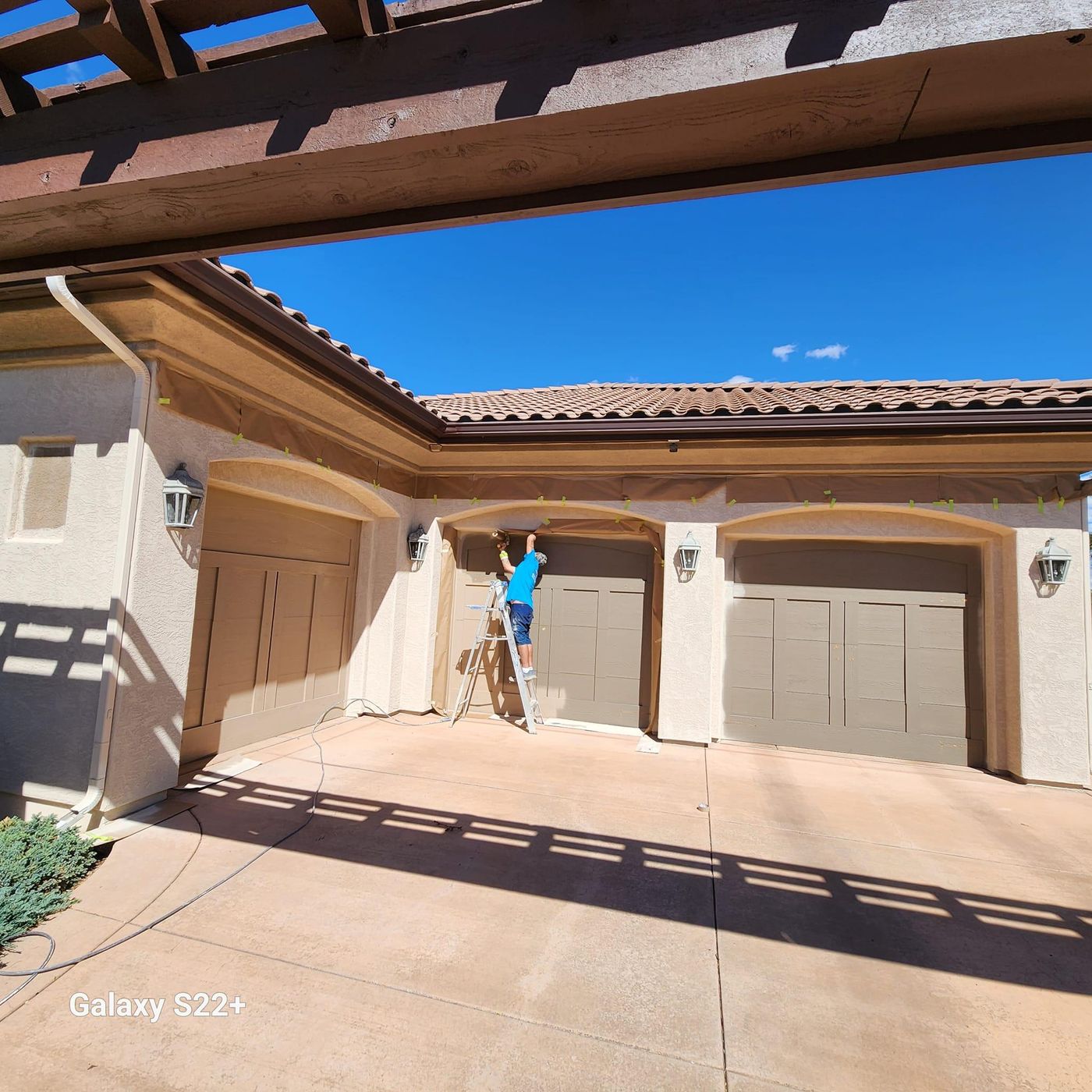 Hoffmann&rsquo;s painter on a ladder finishing a stucco three-car garage under a timber pergola