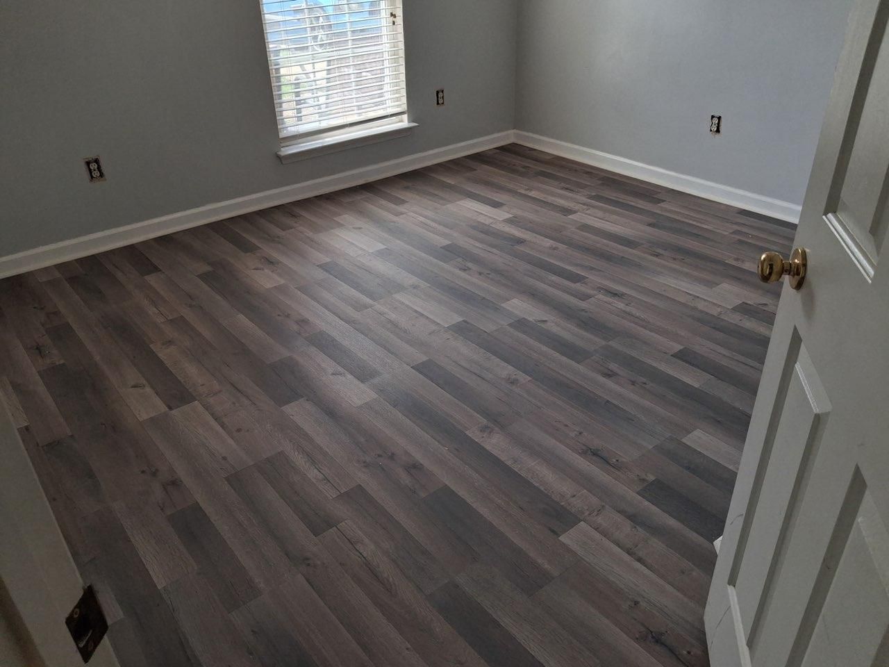 Gray plank luxury vinyl floor in a bedroom with new white baseboard