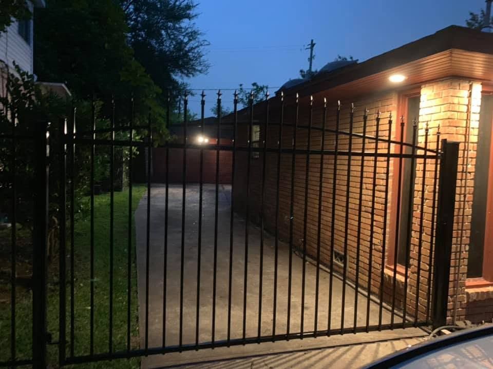 Iron drive gate at dusk with porch lights on