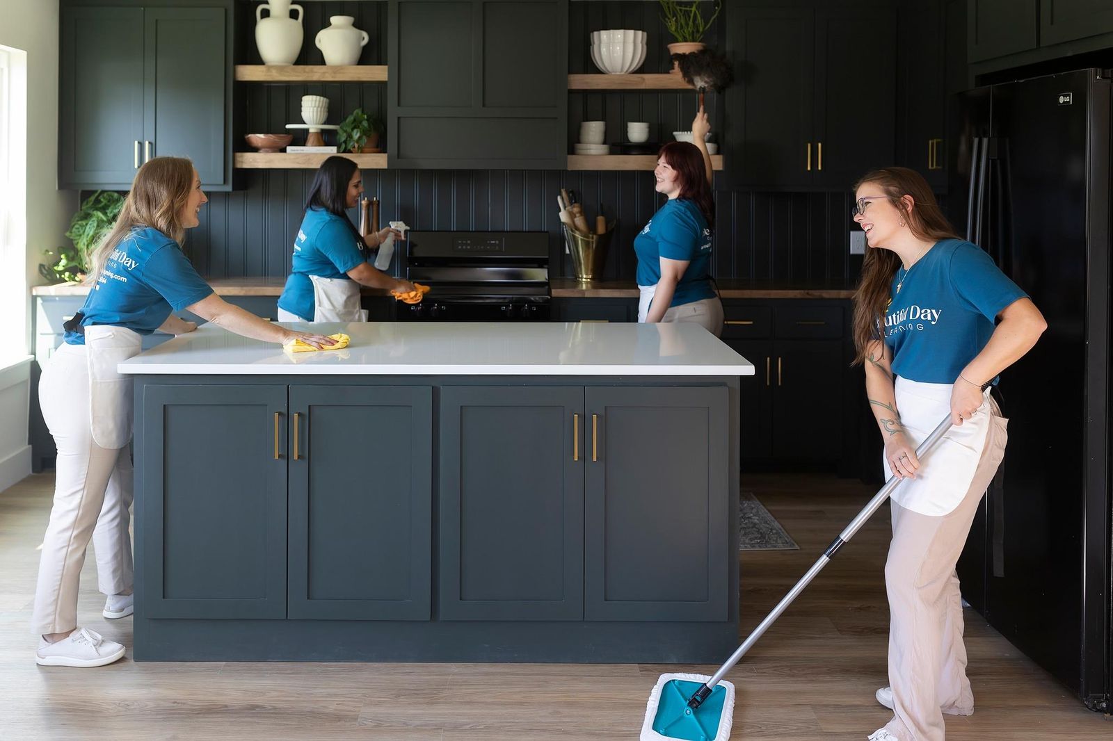A Beautiful Day Cleaning team wiping a kitchen island, dusting shelves and mopping the floor