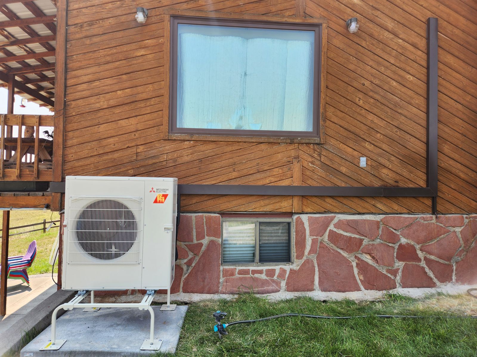 Mitsubishi outdoor unit on a wall stand against cedar siding and a stone foundation