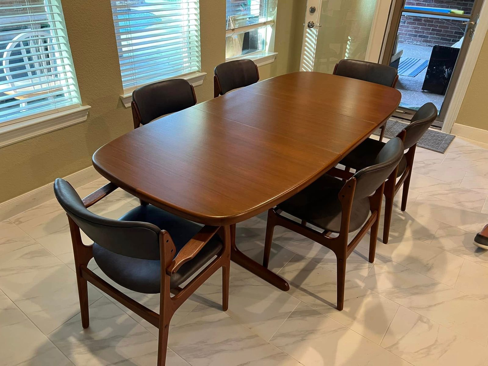 Mid-century teak dining table with six leather-seat chairs on a tile floor