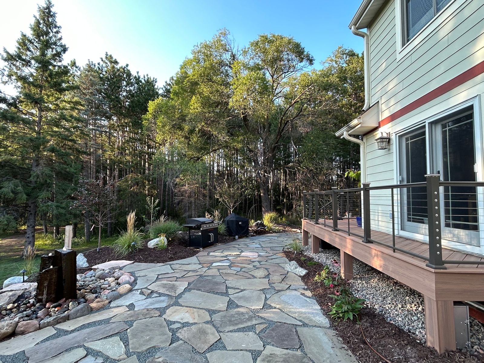 Flagstone patio leading to a deck with cable railing