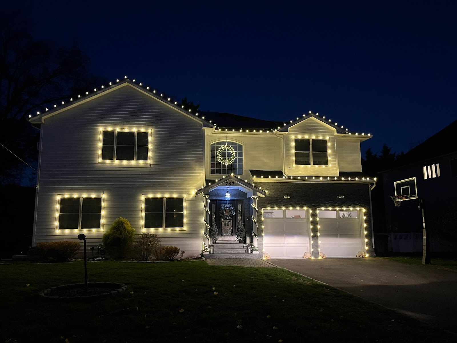 Two-story home outlined in warm white Christmas lights along the roofline, windows and garage, installed by Innovation Power Washing