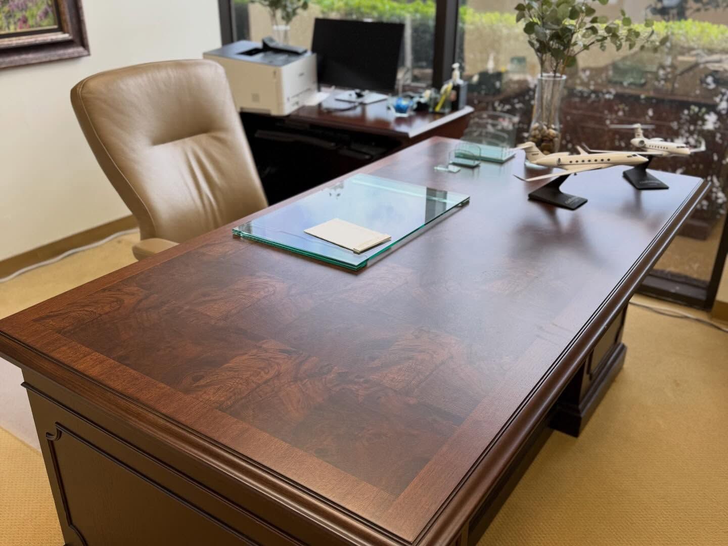 Large executive desk with a glossy wood-veneer top and a glass desk pad in an office