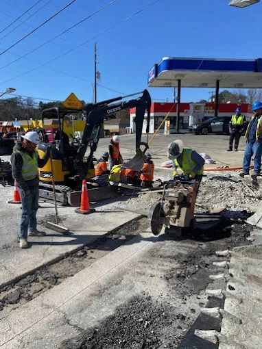 V Construction crew in hard hats and hi-vis saw-cutting and finishing concrete at a commercial gas station site
