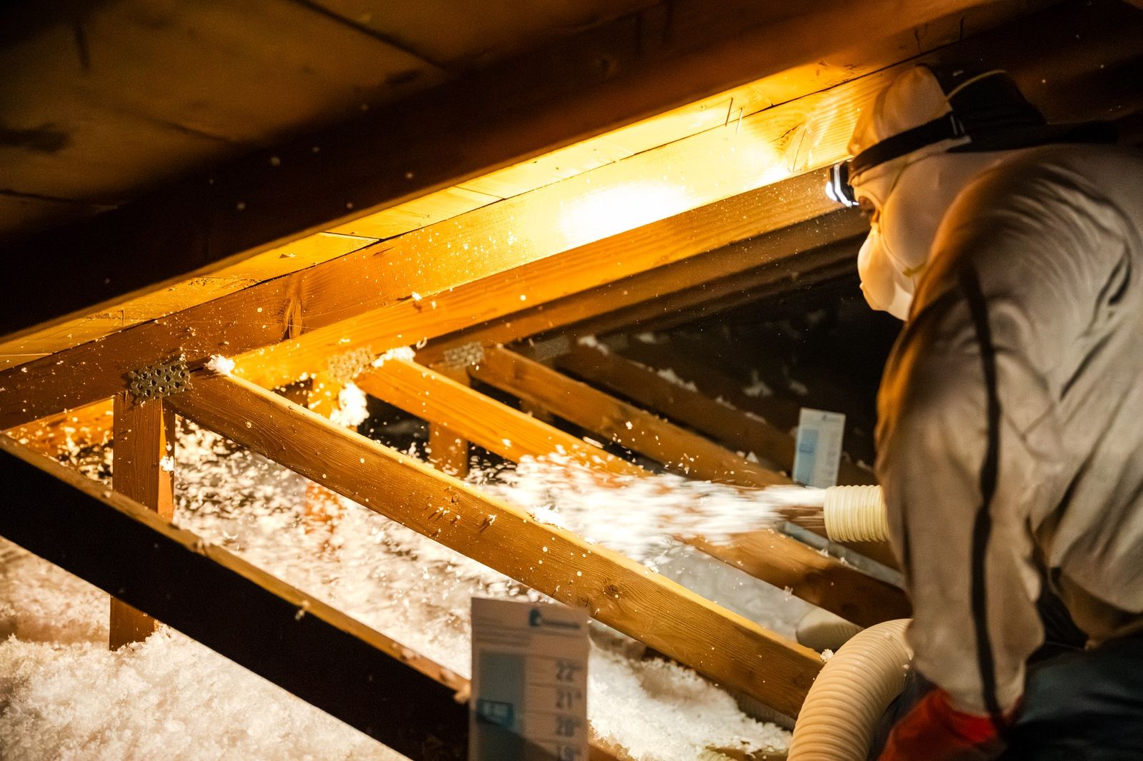 Foam Pro Insulation technician kneeling in a Phoenix attic blowing insulation by headlamp