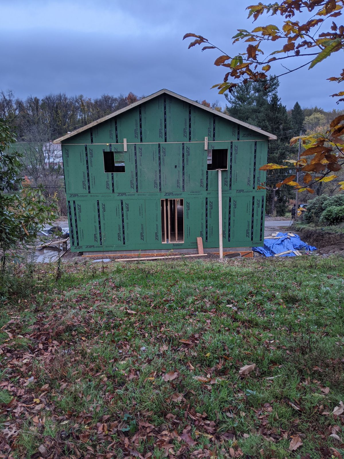 Two-story house frame wrapped in green sheathing among autumn trees
