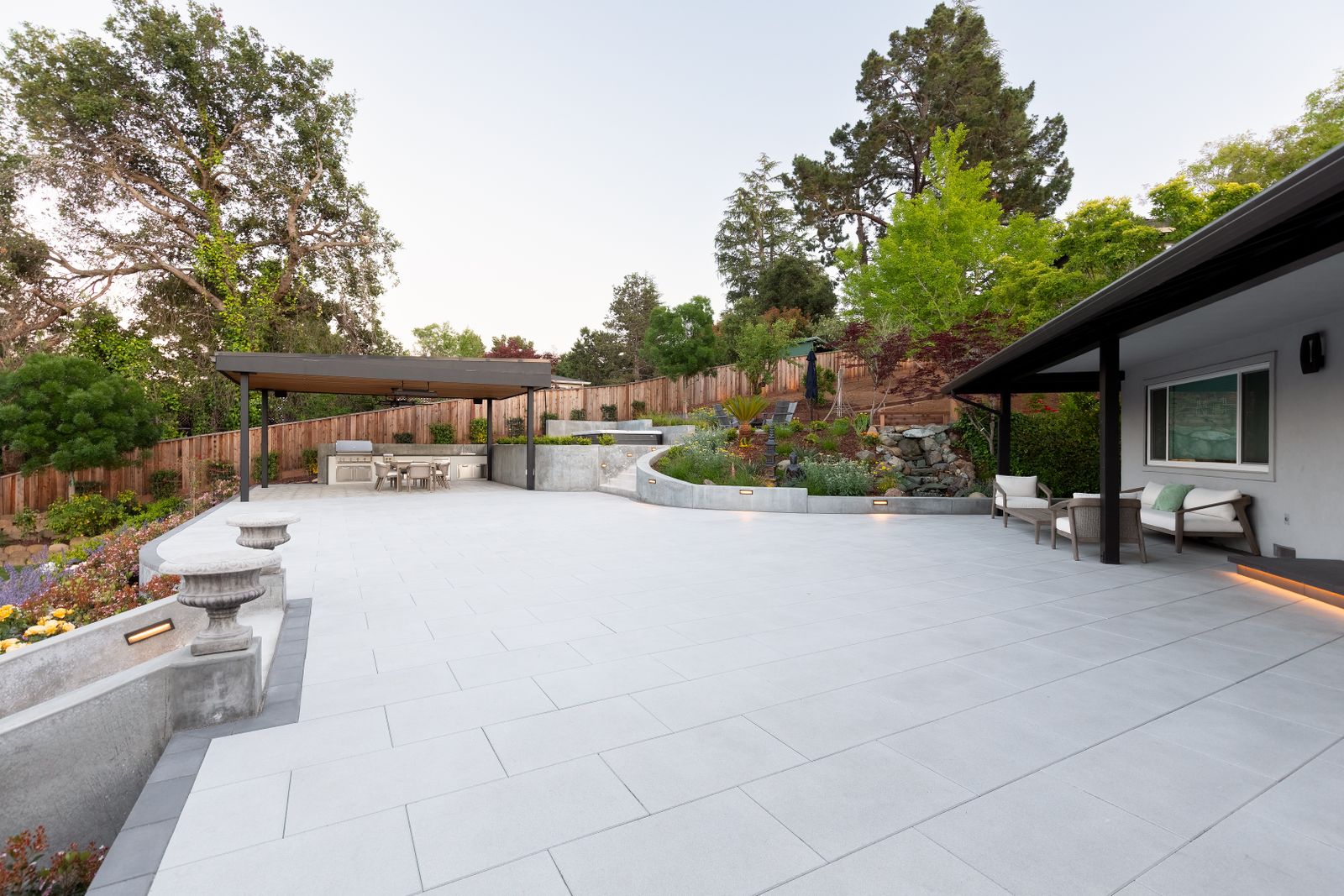 The finished terrace — large-format paving, a curved concrete planter and a timber-topped shade structure