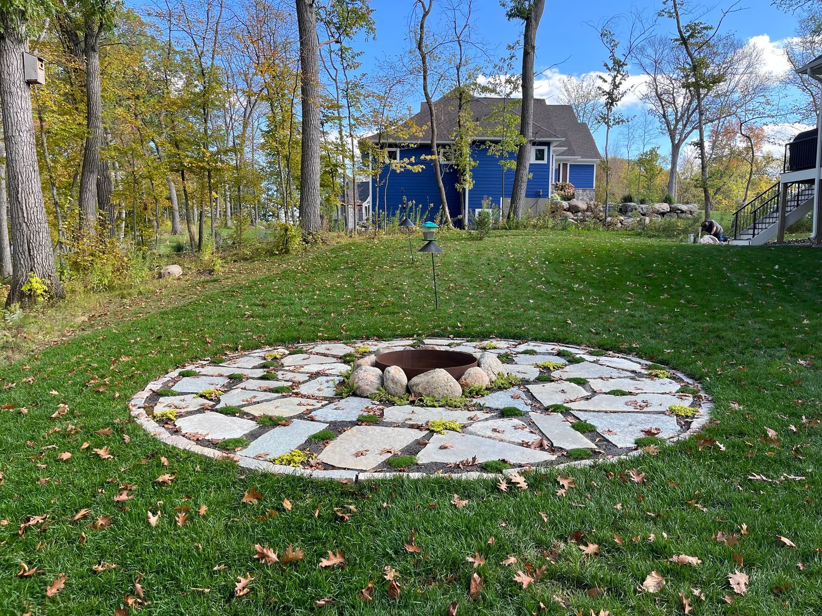 Flagstone fire pit ring set into a wooded backyard lawn in fall