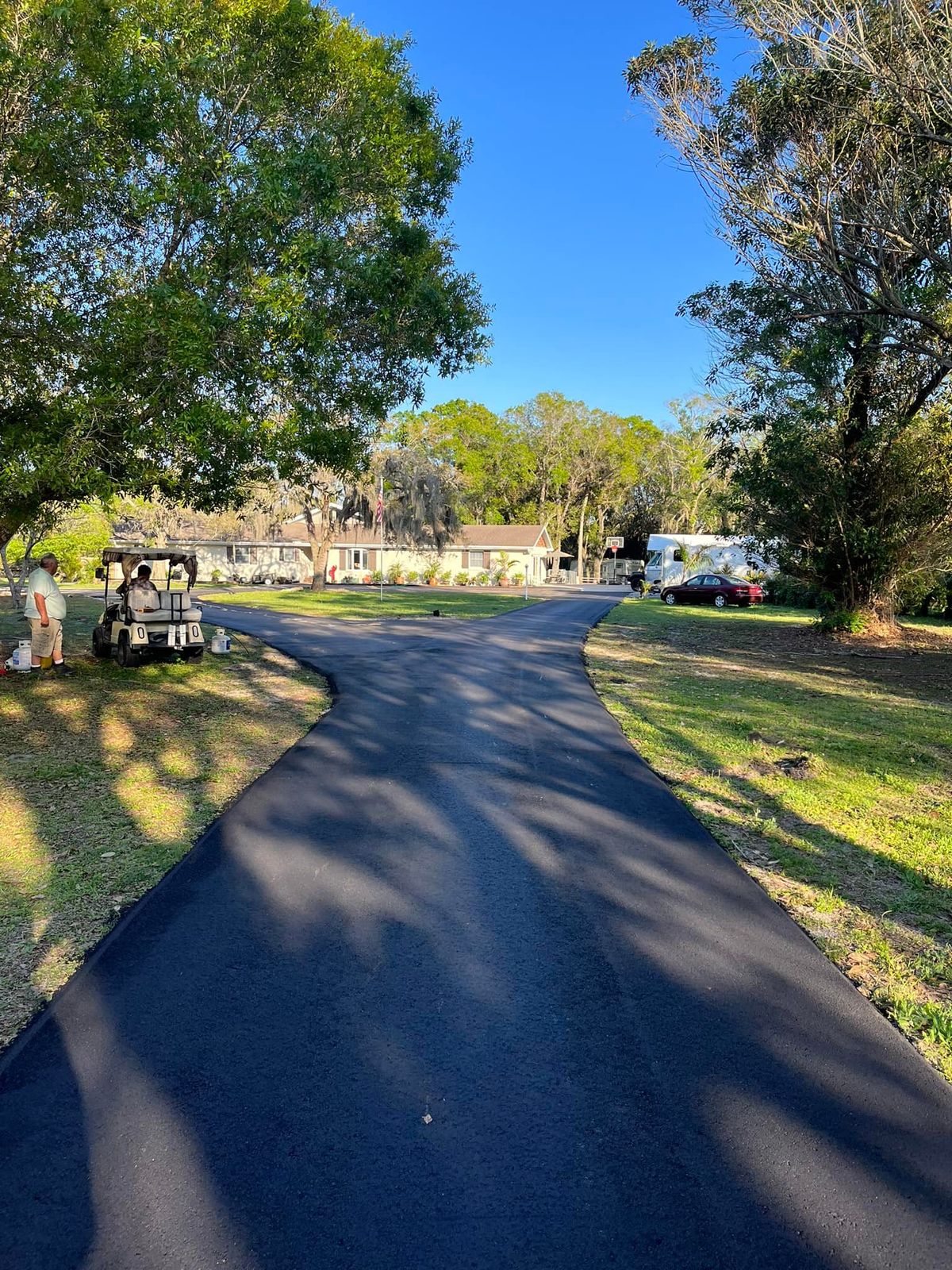 Freshly paved jet black driveway curving past a lawn in the sun
