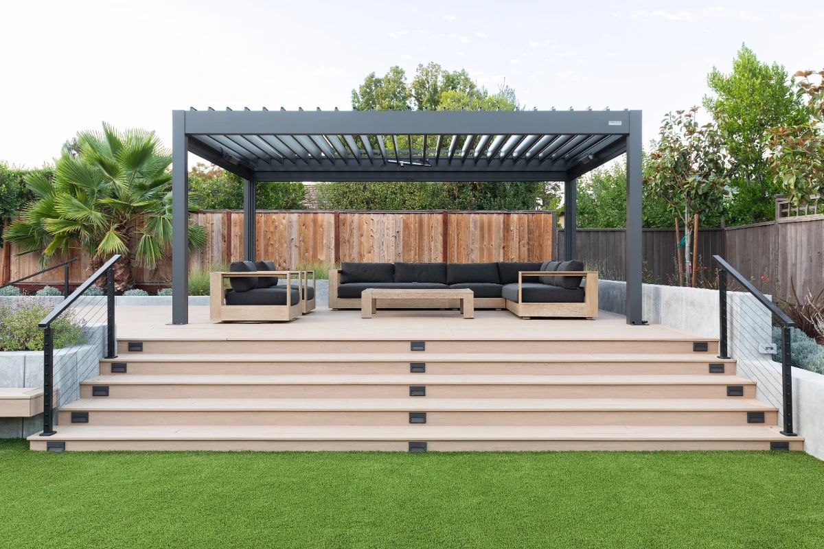 A louvered pergola over a composite deck with lounge seating, steps down to the lawn