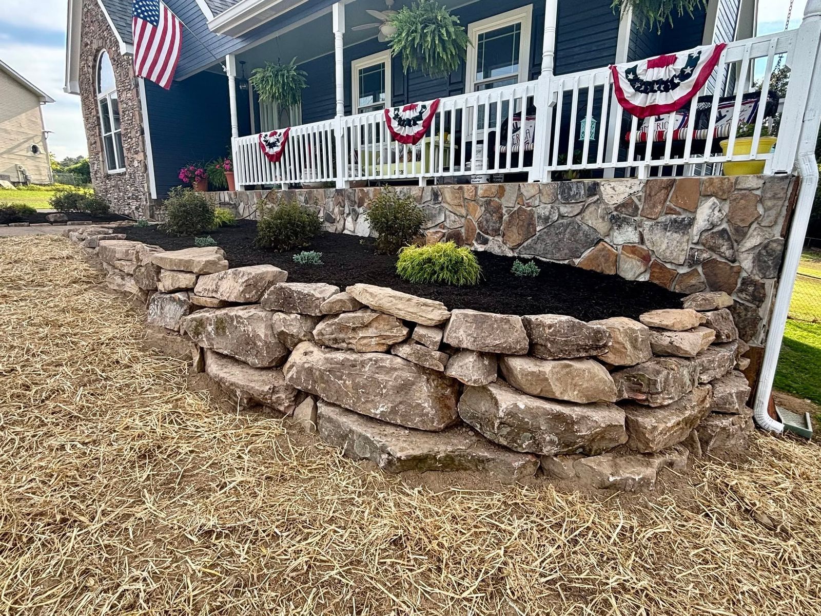 Natural stacked stone retaining wall in front of a porch with new plantings