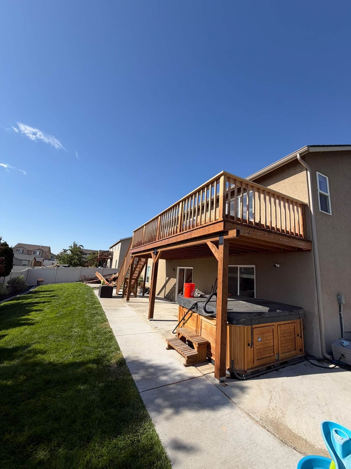 Raised stained deck with a railing above a hot tub patio under a blue sky
