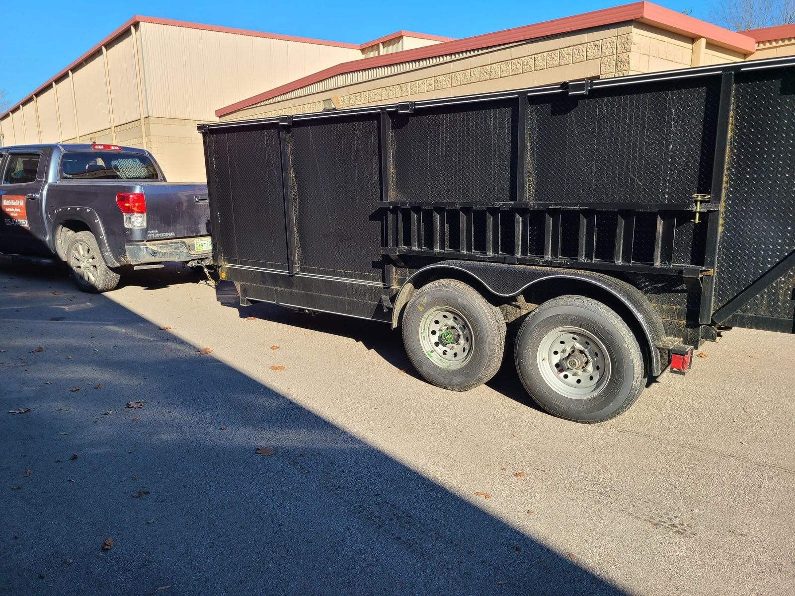 Black high-side dump trailer hitched to a Matt's Haul it All pickup in a parking lot