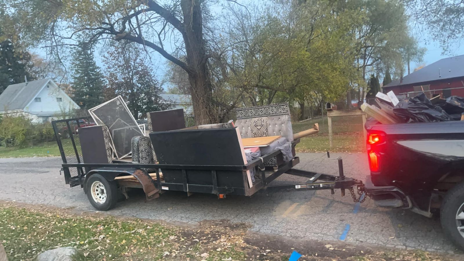 Utility trailer loaded with scrap behind a pickup truck on a residential street