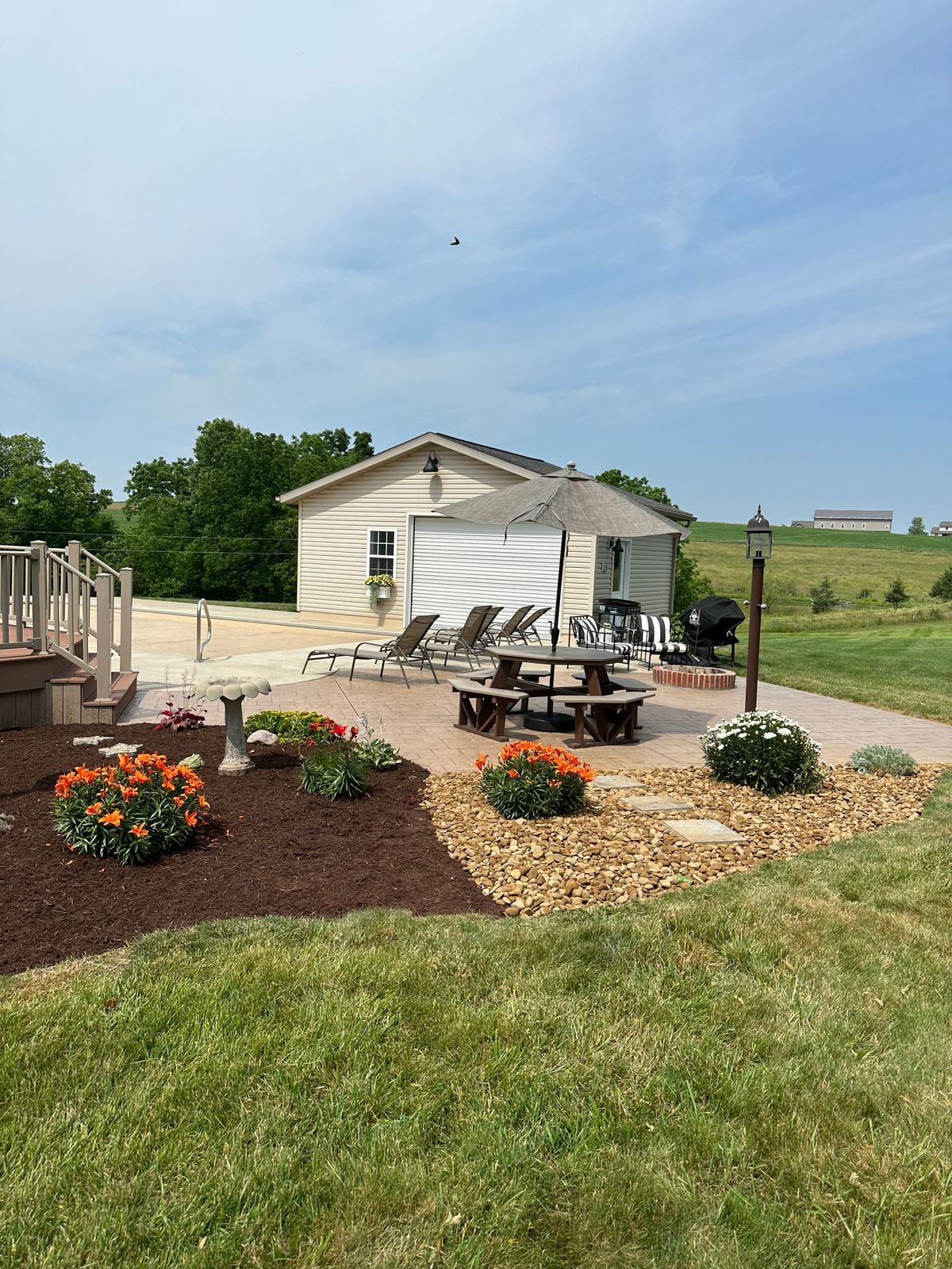 Backyard patio with lounge chairs and a picnic table beside mulch beds with orange flowers