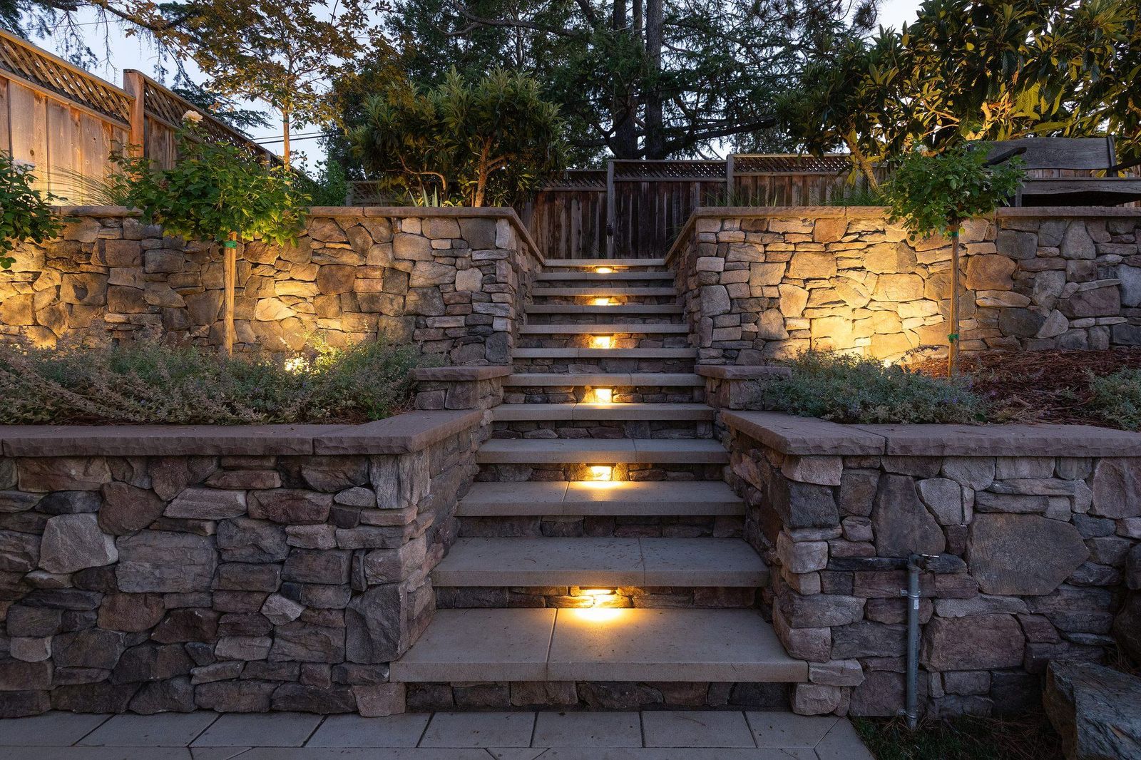 Stacked natural stone retaining walls with a broad stone stair, lighting set into the risers