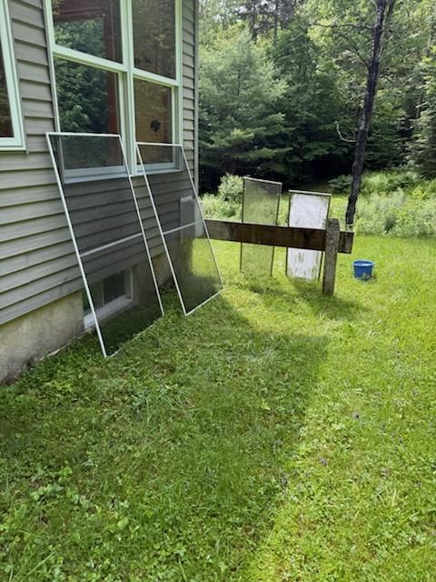 Window screens and glass panels leaning against the siding of a house on a lawn