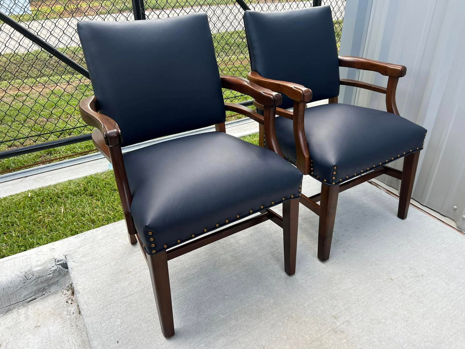 Two wood-frame armchairs with navy leather seats and nailhead trim