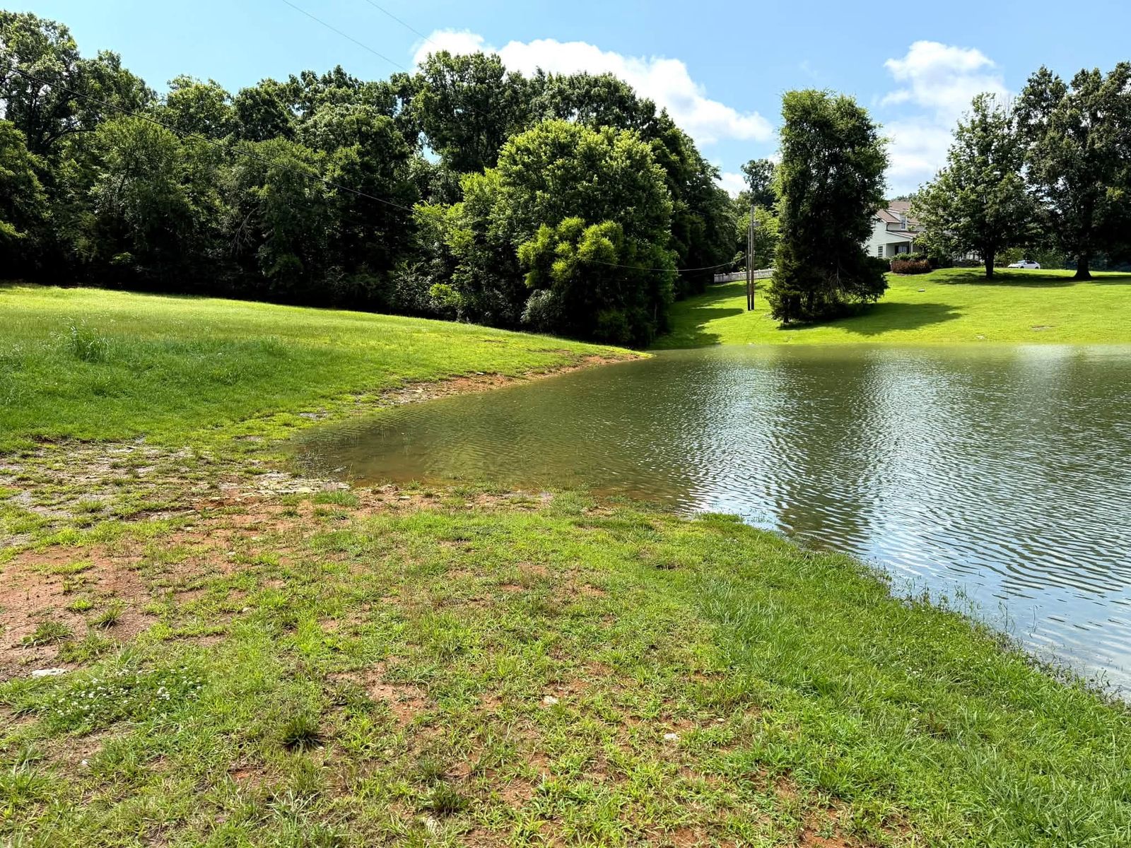 Finished pond with open water and a mowed green bank, with a house in the distance