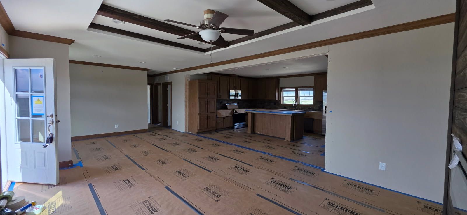 Finished living room with a tray ceiling and wood beams, floor protection paper still down after the drywall and paint work